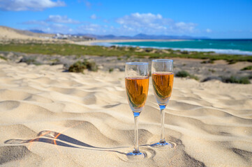 Two glasses of rose champagne or cava sparkling wine served on white sandy tropical beach with...