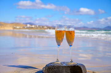 Two glasses of rose champagne or cava sparkling wine served on white sandy tropical beach and blue ocean water, romantic vacation, winter sun on Fuerteventura, Canary, Spain