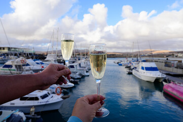 Everyday party, hands with glasses of cava or champagne sparkling wine in yacht harbour of Caleta Fuste, Fuerteventura, Canary islands vacation, Spain