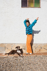 hunting dog and young latin girl in colorful clothes, saturated blue argyle sweater and orange pants, white stucco wall background outside, light sunny day. Listen music with headphones and dancing