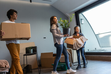 Mixed race family moving into their new home. They're carrying cardboard full of their accessories.	