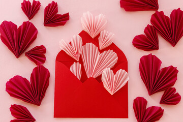 Valentines day flat lay. Stylish envelope with pink and red hearts composition on pink paper background. Creative modern valentine hearts cutouts. Happy Valentine's day! Love letter