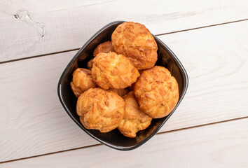 Sweet and tasty chouquettes in a black ceramic plate, close-up, on a painted wooden table, top view.