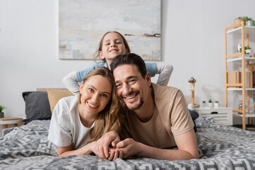 portrait of happy child behind positive parents looking at camera while resting in bedroom.