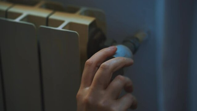 Female hand adjusting thermostat to turn on the radiator heater at home.