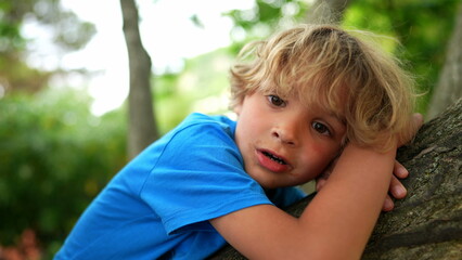 Child leaning on trunk tree. Kid connected with nature