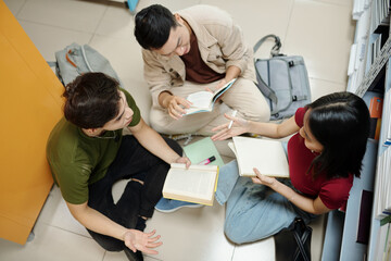 Obraz premium Group of students sitting on floor in school library and discussing ideas for project