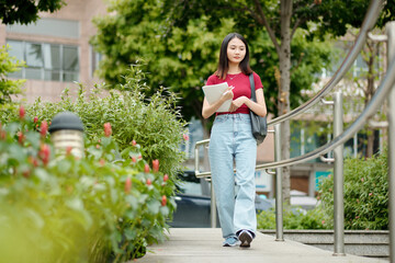 Pensive high school student with textbook in hands walking home after classes