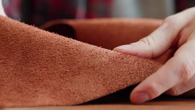 Craftsman touching leather close-up, production of handmade accessories made of genuine or artificial animal skin. Hide material on workplace, quality control.