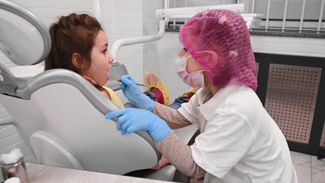 Little kids girls playing dentist hygienist, treating each other, doing teeth examination in the dentist's office. Pediatric dentistry. The concept of familiarization with the future profession
