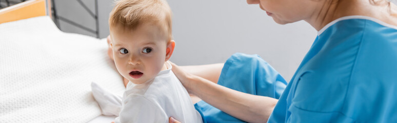toddler girl looking away while sitting with open mouth near mother on hospital bed, banner.