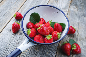 Reife rote Erdbeeren aus biologischem Anbau angeboten als close-up in einem rustikalen Abtropfsieb auf altem verblichenem Holz