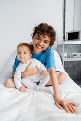 excited woman laughing with closed eyes and hugging baby on bed in hospital ward.