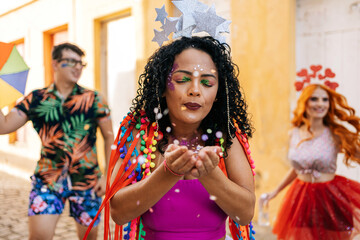 Fototapeta na wymiar Brazilian Carnival. Young woman enjoying the carnival party blowing confetti