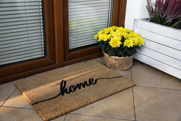 Doormat with word Home and flowers near entrance outdoors