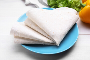 Delicious folded Armenian lavash and fresh vegetables on white wooden table, closeup