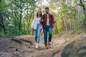 A couple is hiking and chatting about interesting topics, surrounded by breathtaking nature and greenery. Trekking poles are helping them with the bumpy trail.