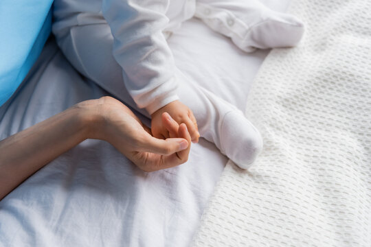 top view of cropped woman holding hand of little girl in romper sitting on hospital bed.