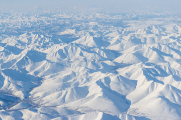 Obraz premium Aerial view of snow-capped mountains. Winter snowy mountain landscape. Air travel to the far North of Russia. Kolyma Mountains, Magadan Region, Siberia, Russian Far East. Great for the background.