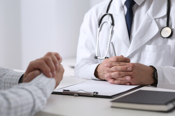 Doctor consulting senior patient at white table in clinic, closeup