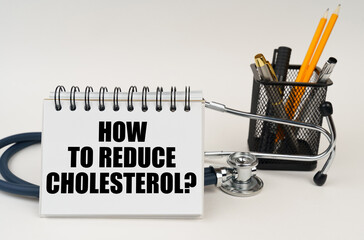 On the table are office supplies, a stethoscope and a notepad with the inscription - How to Reduce Cholesterol