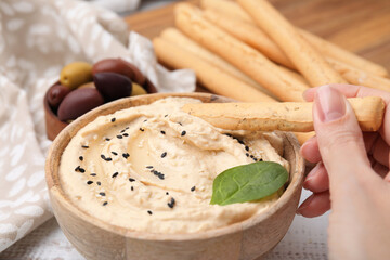 Woman dipping tasty grissini stick into hummus at white wooden table, closeup