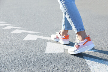 Planning future. Woman walking on drawn marks on road, closeup. White arrows showing direction of...