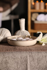 Spa composition with burning candles, lily flower and herbal bags on massage table in wellness center