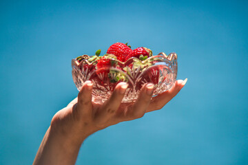 Manos sosteniendo un boul de vidrio con deliciosas frutillas dentro, sol radiante