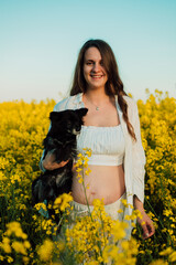 A pregnant woman with a small black dog in nature. Rapeseed field