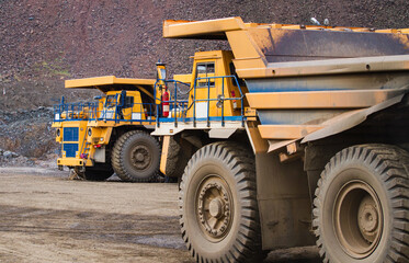 Large yellow dump trucks engaged in the transportation of rock mass in the quarry for mining. Machinery and equipment for iron ore mining
