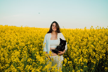 Fototapeta premium A pregnant woman with a small black dog in nature. Rapeseed field