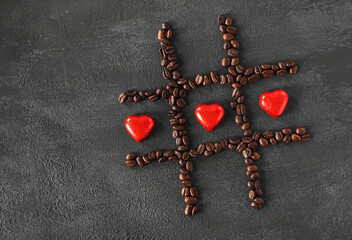Candy in the form of hearts in a rack of coffee beans on black stone background, top view copy space