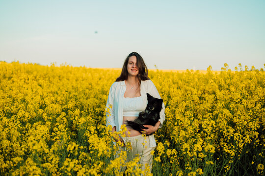 A pregnant woman with a small black dog in nature. Rapeseed field