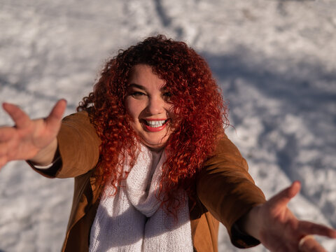 Portrait of a fat red-haired woman stretching out her arms for hugs on a walk in winter. 