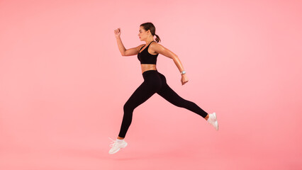 Fototapeta na wymiar Motivated Sporty Young Woman Running In Mid-Air Over Pink Background