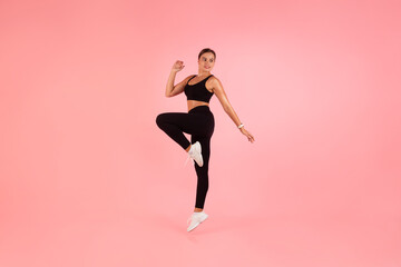 Fototapeta na wymiar Beautiful Sporty Woman In Fitwear Jumping Over Pink Studio Background