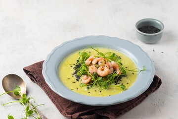 Green pea soup with pea microgreens, black sesame and shrimp in a gray plate on a light concrete background. Soup recipes.
