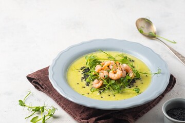 Green pea soup with pea microgreens, black sesame and shrimp in a gray plate on a light concrete background. Soup recipes.