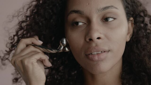 CU Headshot portrait of beautiful 20s African-American Black female cosmetic face roller against brown background, no make-up, clean skin. Shot with ARRI Alexa Mini LF