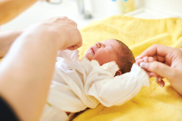 Fototapeta na wymiar Parents together dressing newborn baby after bath
