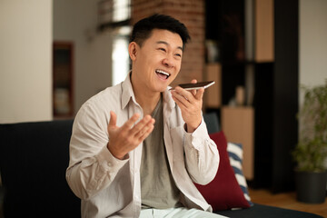 Portrait of happy asian man holding cellphone near mouth and recording message, using digital assistance app