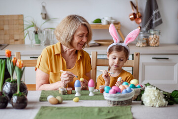 Happy easter family elderly grandmother and little granddaughter with rabbit ears are preparing for the holiday to paint eggs