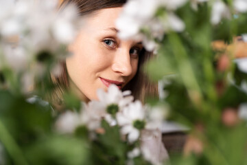 Smiling face of a beautiful young woman surrounded by white flowers and green leaves