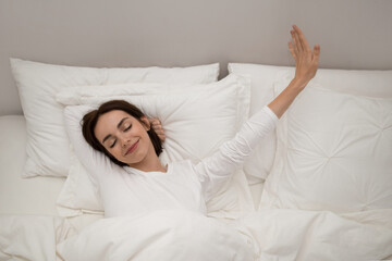 Joyful young lady stretching in bed after waking up