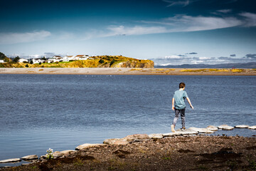 Boy jumping rock to rock at low tide playing on a beach at low tide at Chance Cove Newfoundland Canada.