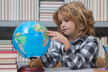 School pupil looking at globe in library, geography lesson. School child studying in classroom at elementary school. Kid studying on lesson in class at elementary school.