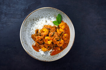 Traditional spicy Indian prawn Madras curry Rogan Josh with king prawns and basmati rice served as top view in a Nordic design bowl with copy space