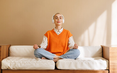 Relaxed young woman in wireless headphonesmeditating on sofa