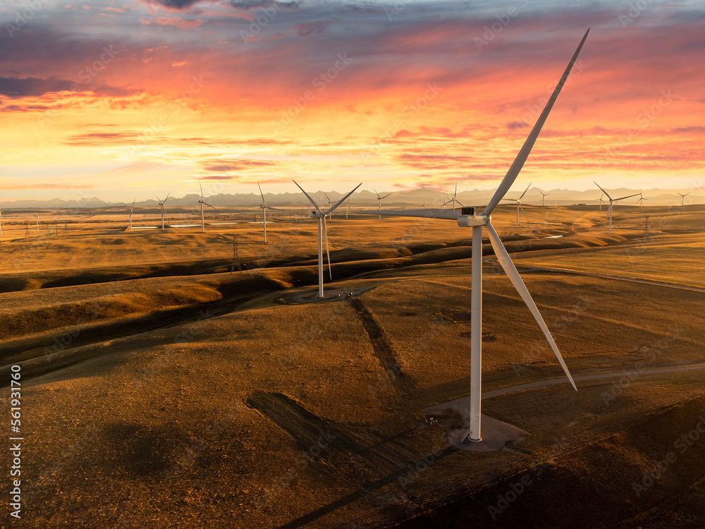 Wall mural Aerial sunset windmills producing sustainable energy over natural grasslands with mountains at background near Pincher Creek Alberta Canada under a colourful dramatic sky.